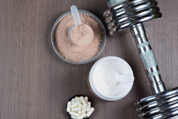 Proteína de soro de leite em um balde de medição, aminoácidos, cápsulas esportivas e um halteres de metal em um espaço de cópia de fundo de madeira — Fotografia de Stock