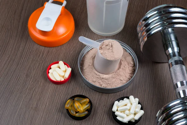 Peynir altı suyu proteini bir metal dumbbell ve shaker ahşap arka plan üzerinde ölçüm bir kova
