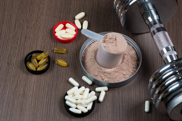 Ahşap arka plan üzerinde metal bir dumbbell ile ölçüm bir kova içinde peynir altı suyu proteini