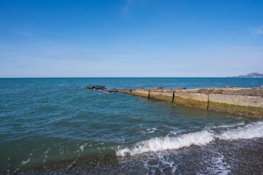 Deniz manzarası, çakıl plaj, beton İskelesi, dağlar ve şehir içinde belgili tanımlık geçmiş. Deniz arka plan