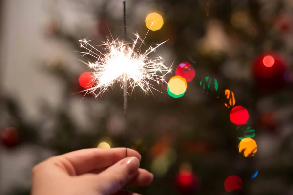  Bir kadın eli ışıklı bir Bengal ateşi Noel ağacı karşı tutar..