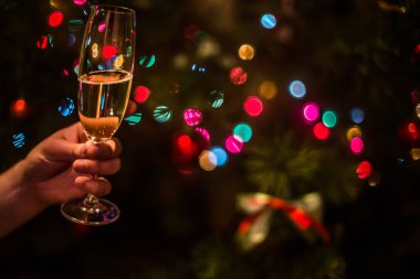 Elinde şampanya olan bir bardak Noel ağacı arka planında