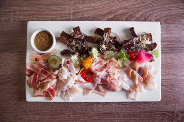 Soğuk aperatif: jambon, göğüs eti tuzlu, samanla tütsülenmiş göğüs eti, pastırma. Hardal sosu ve fırında soğanla servis edilir. Kahverengi arka plan. Üst Manzara. Ahşap masa
