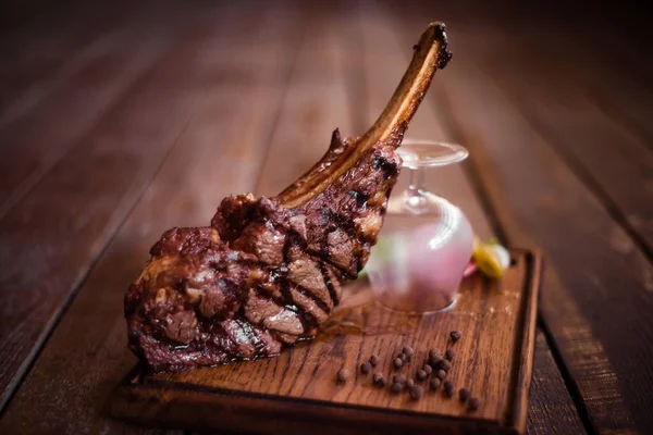 Delicious juicy steak on a sugar bone, cooked on the grill. The steak is served on a Board and decorated with a glass. Cawboy steak.