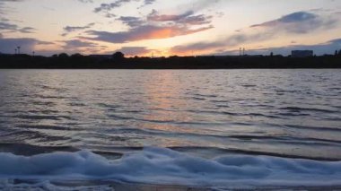 Altın saat, su manzarası. Gölün kıyısında bir sürü beyaz tüylü köpük var. Göl dalgaları tarafından yaratılan sörf, renkli akşam gökyüzüne karşı. Huzurlu bir gün batımı manzarası.