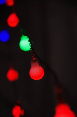 Koyu arkaplanda çok renkli ampulleri olan yeni yıl çelenkleri, yeni yılın çelenkleriyle soyut bir arkaplan