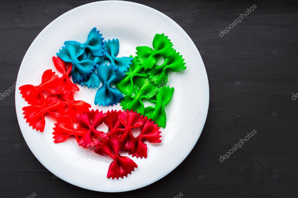 blue, green, red, pink pasta in a white plate on a black wooden background. creative food