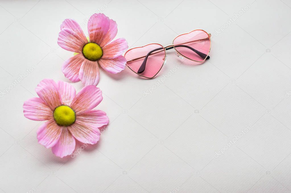 rose-colored glasses in the shape of heart, two pink flowers close-up. pink background. concept summer and relax. flat lay