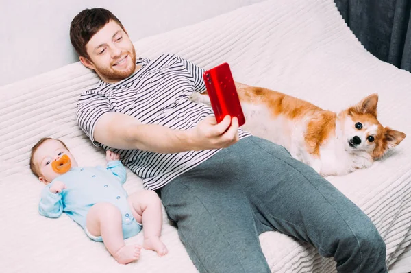 Hombre, niño y perro se toman selfie en la cama . — Foto de Stock