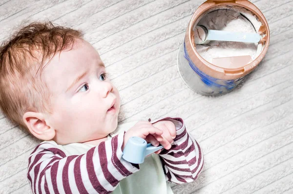 Bebé está acostado cerca de una lata de leche para bebés y lo mira . — Foto de Stock
