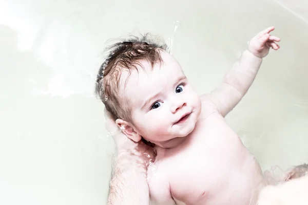 El bebé se baña en el baño. Papá sostiene al bebé en el agua. Bebé sonriendo — Foto de Stock