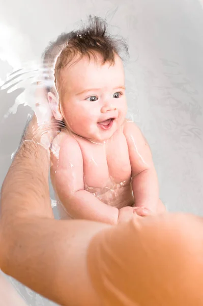 Baby bathes in the bath. Dad holds the baby in the water.Vertical photo — Stock Photo, Image