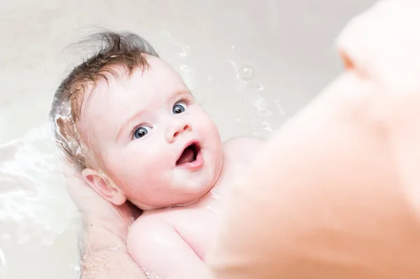 El bebé se baña en el baño. Papá sostiene al bebé en el agua . — Foto de Stock