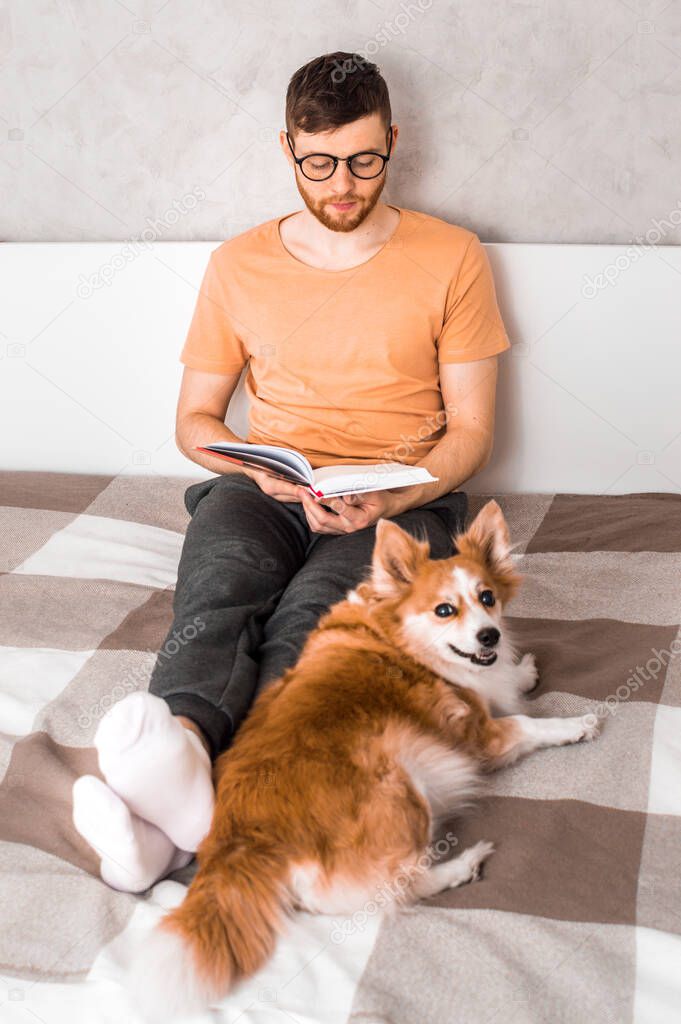 Young man reads a book in bed with his dog. Vertical photo