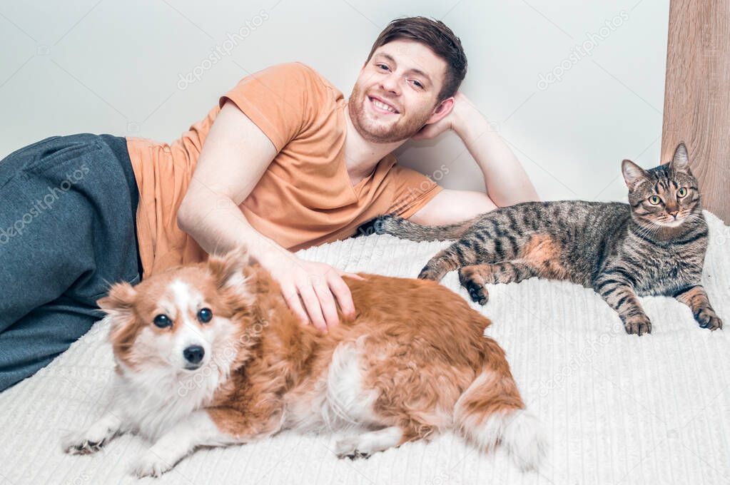 Owner with his dog and cat is hugging on the bed. Pets