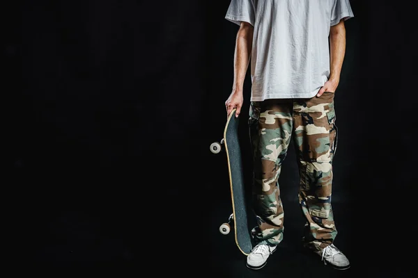 黒の背景にスケート ボードを持つ男 — ストック写真