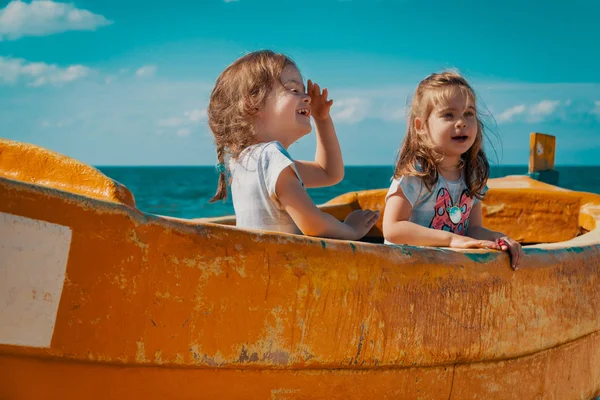 Two girls play in a fishing boat on the beach — Stock Photo, Image