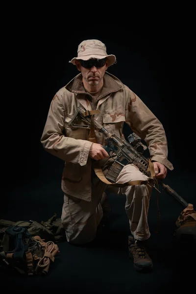 Forças especiais soldado ajoelha-se com um rifle em um fundo preto — Fotografia de Stock