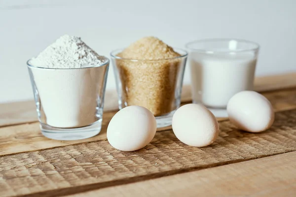 Süt, un, şeker ve hamur yumurta üzerinde ahşap bir masa — Stok fotoğraf