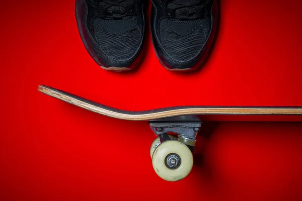 Schoenen en gebruikte skateboard op een rode achtergrond — Stockfoto