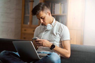 Evdeki gri koltukta dizüstü bilgisayarı olan yakışıklı bir genç. 