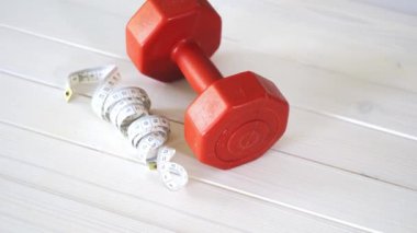 beyaz ahşap masa üzerinde kırmızı fitness dumbbell ve santimetre bant