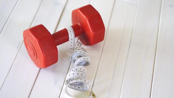 Red fitness dumbbell and centimeter tape on white wooden table — Stock Video