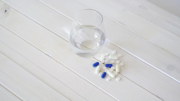 Vaso de agua cristalina y conjunto de píldoras sobre mesa de madera blanca — Vídeo de stock