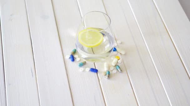 Vaso de agua cristalina con limón y set de píldoras sobre mesa de madera blanca — Vídeos de Stock