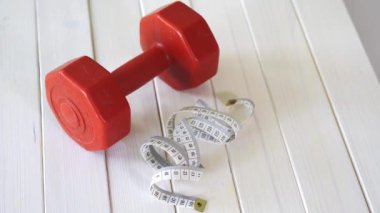 beyaz ahşap masa üzerinde kırmızı fitness dumbbell ve santimetre bant