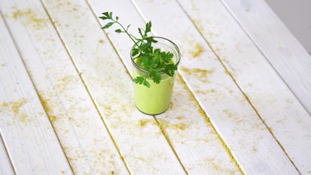 砂と白い木製のテーブルの上にパセリの小枝と健康的な緑のフルーツとビーガンカクテル — ストック動画