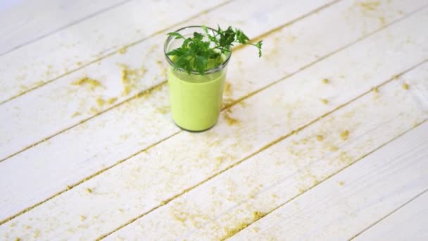 Healthy green fruit and vegan cocktail with sprig of parsley on white wooden table with sand — Stock Video