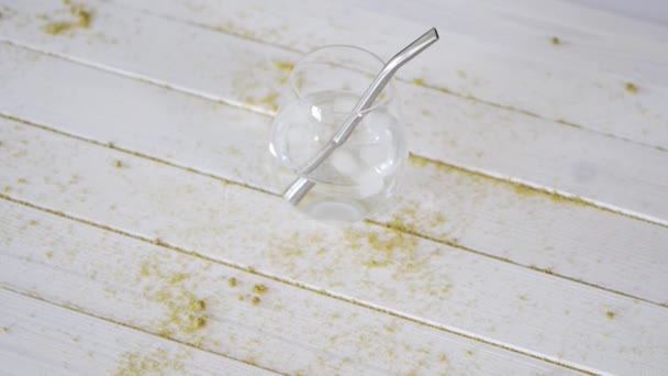 Szkło z kryształową wodą ze słomy tytanowej i kostki lodu na stole z piaskiem — Wideo stockowe