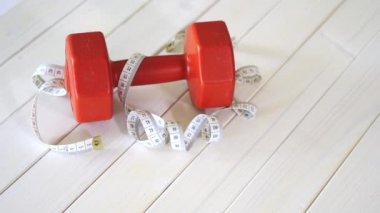 beyaz ahşap masa üzerinde kırmızı fitness dumbbell ve santimetre bant