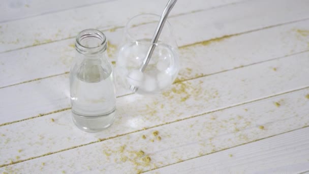 Sklo krystalové vody s titanovou slámou a láhev na dřevěném stole s pískem — Stock video