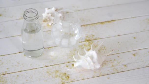 Glas med vatten och vita snäckskal på träbord med sand — Stockvideo