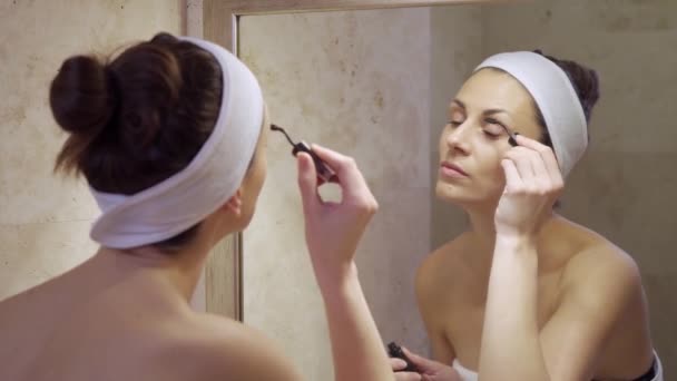 Vacker ung kvinna målar ögonfransar i spegeln i badrummet — Stockvideo