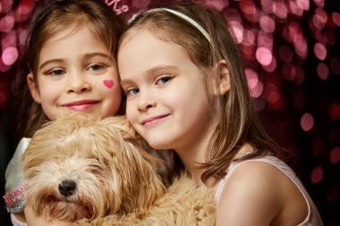 Köpekli iki sevimli kız parlak arka planda poz veriyorlar.