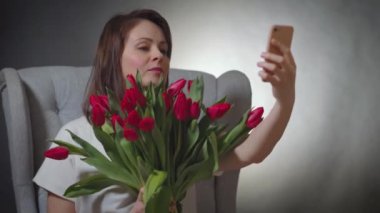 Bir buket kırmızı lale ile güzel bir selfie çeker sandalyede