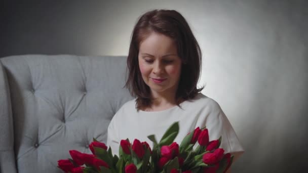 Beautiful woman smelling a bouquet of red tulips on chair — Stock Video