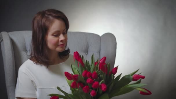 Beautiful woman smelling a bouquet of red tulips on chair — Stock Video