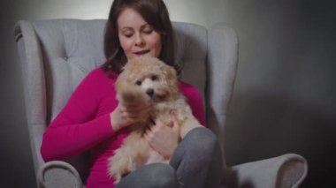 Güzel bir kadın sandalyede küçük bir köpek yavrusuyla oynuyor.