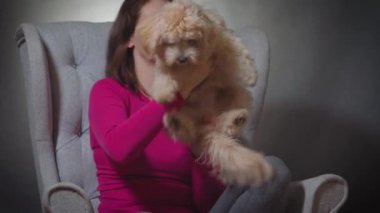 Güzel bir kadın sandalyede küçük bir köpek yavrusuyla oynuyor.