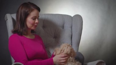 Güzel bir kadın sandalyede küçük bir köpek yavrusuyla oynuyor.