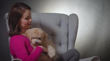 Güzel bir kadın sandalyede küçük bir köpek yavrusuyla oynuyor.
