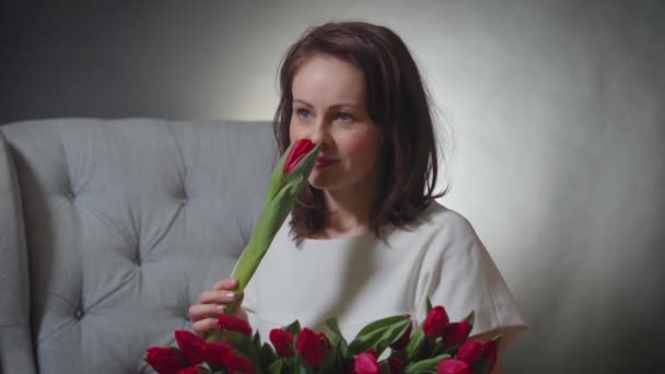 Hermosa mujer oliendo un ramo de tulipanes rojos en la silla — Vídeos de Stock