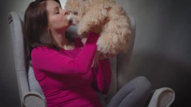 Güzel bir kadın sandalyede küçük bir köpek yavrusuyla oynuyor.