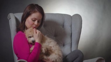 Güzel bir kadın sandalyede küçük bir köpek yavrusuyla oynuyor.