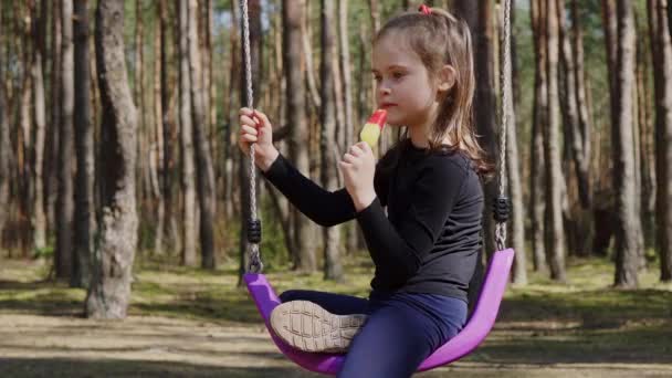 Little girl eats ice cream on a swing in the spring forest — Stock Video