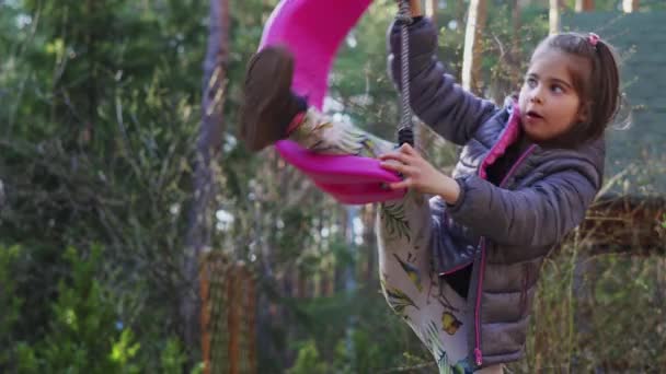 Маленькая девочка крутится на качелях в весеннем лесу — стоковое видео
